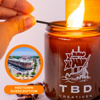 Candle being lit from a match, with 'TBD Creatives' branding and a small inset image of a building.