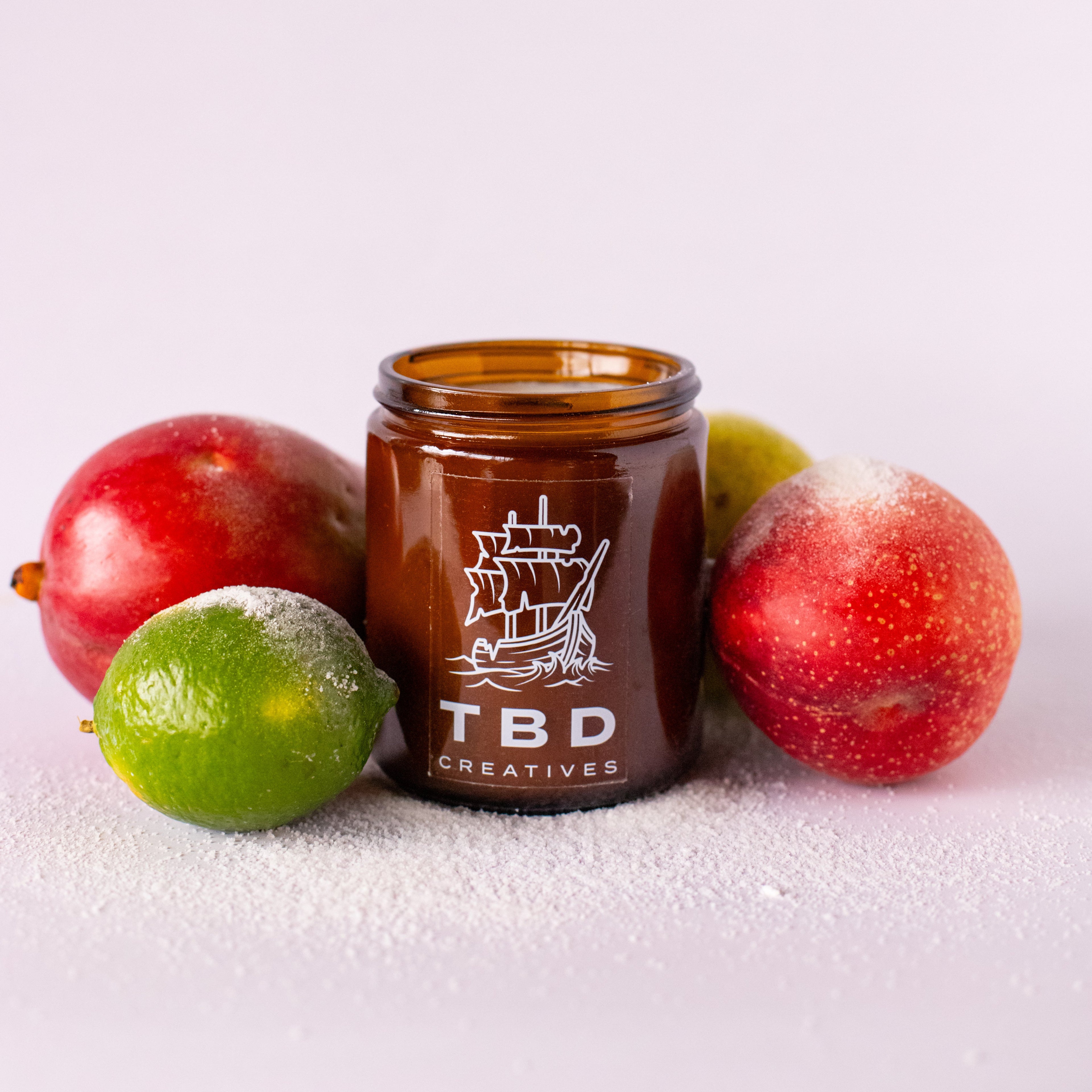 Brown jar with 'TBD Creatives' logo surrounded by fruits on a white background