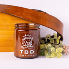 Brown jar with 'TBD Creatives' logo on a white background with a guitar and flowers.