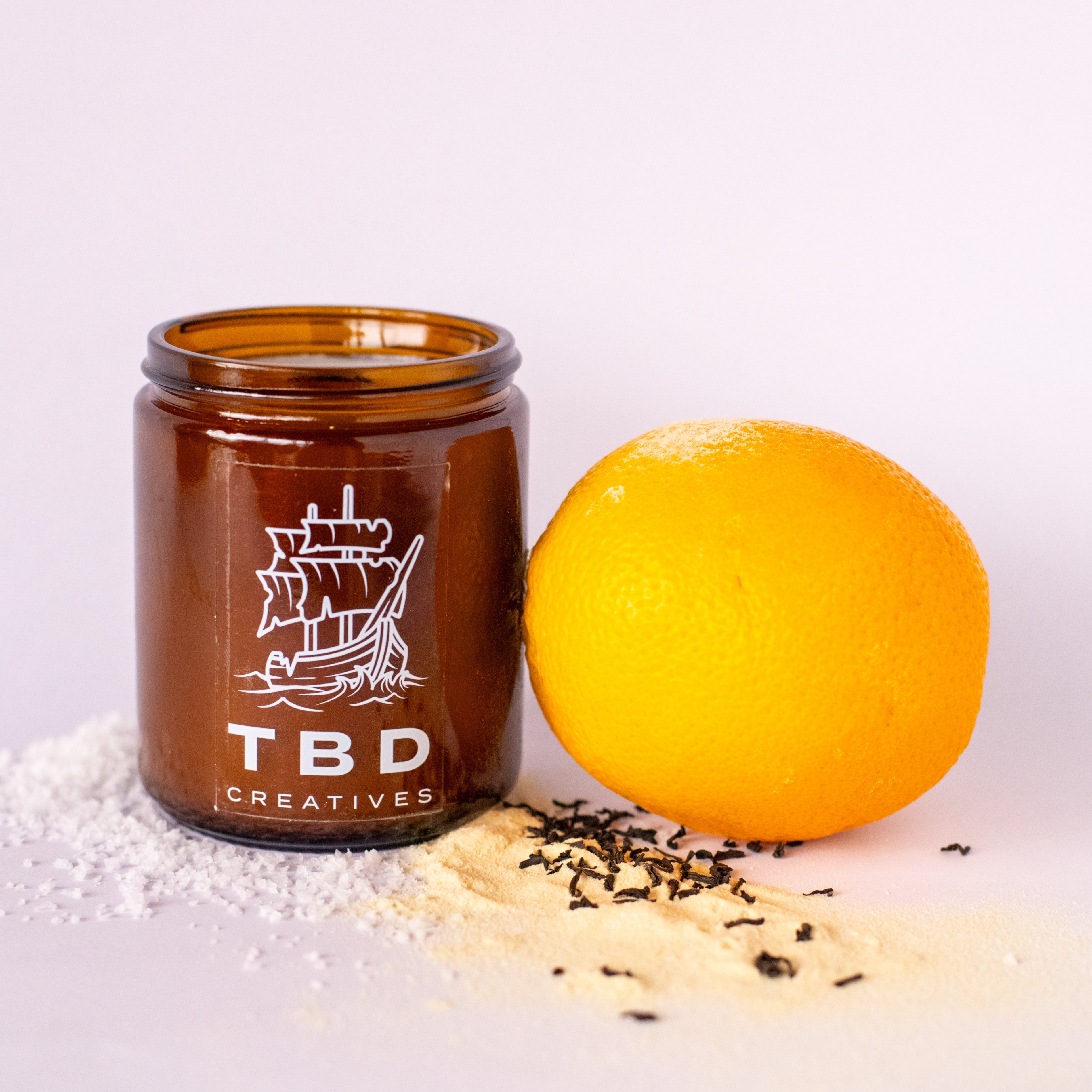 Jar with 'TBD Creatives' logo next to an orange on a light background
