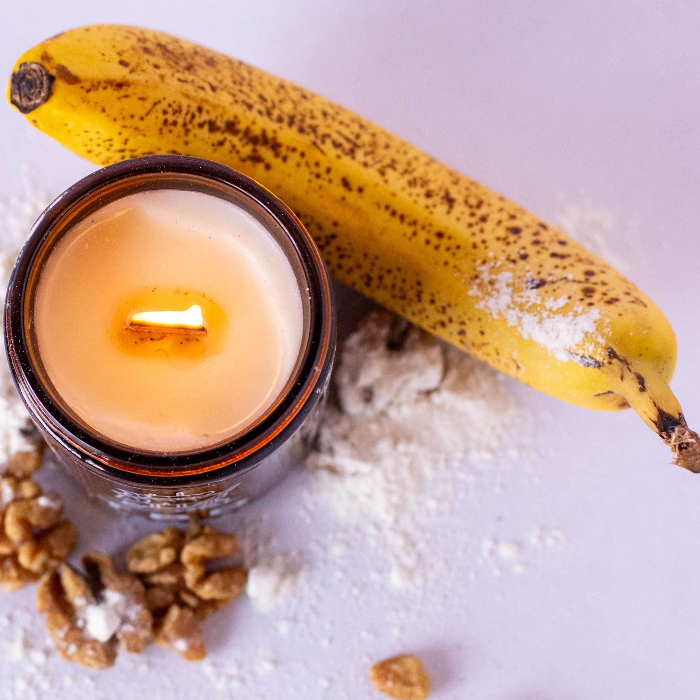 Candle in a glass jar with a banana and walnuts on a light background