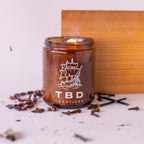 Candle in a glass jar with 'TBD Creatives' branding on a light background