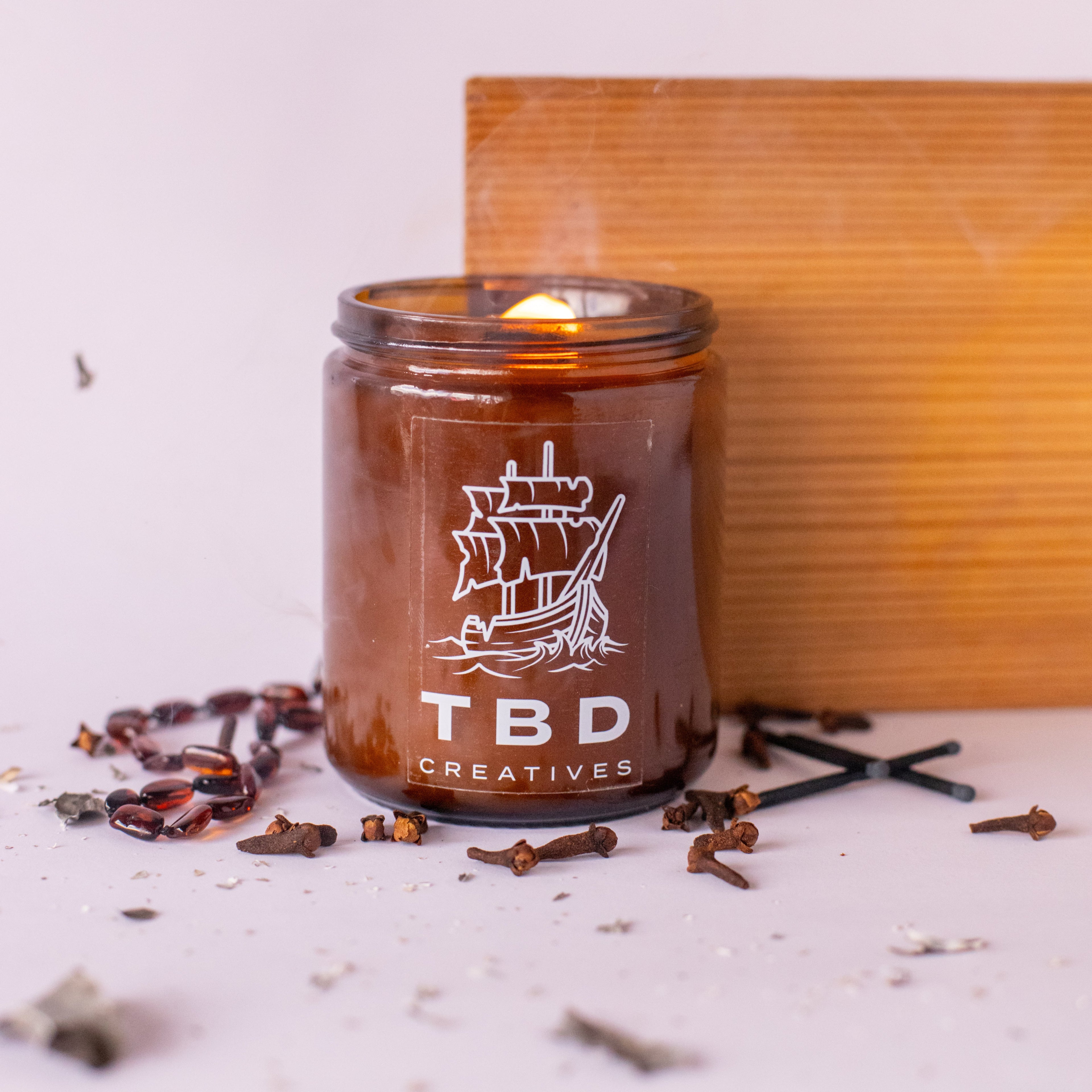 Candle in a glass jar with 'TBD Creatives' branding on a light background