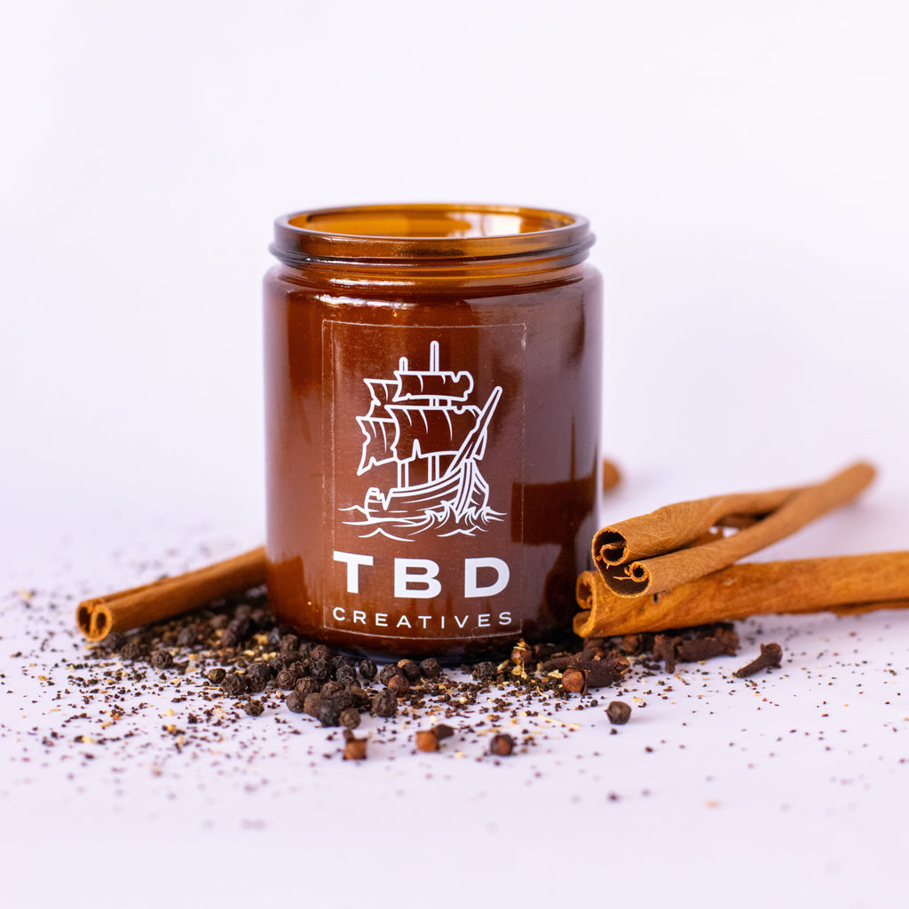 Brown jar with 'TBD Creatives' branding on a white background with cinnamon sticks and tea leaves.