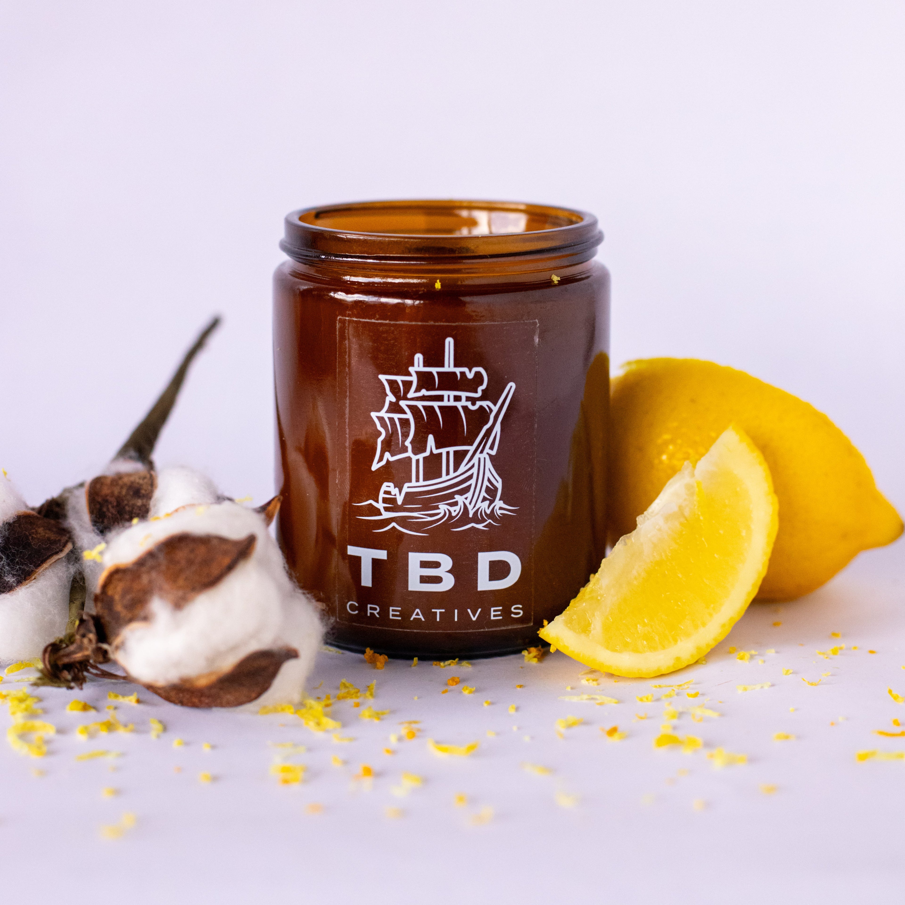 Brown jar with 'TBD Creatives' logo on a white background with lemons and cotton.