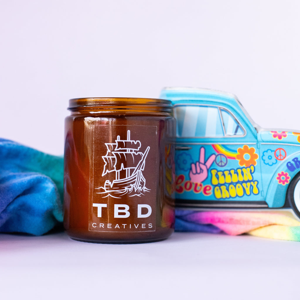 Brown candle with 'TBD Creatives' branding next to a colorful toy truck on a white background