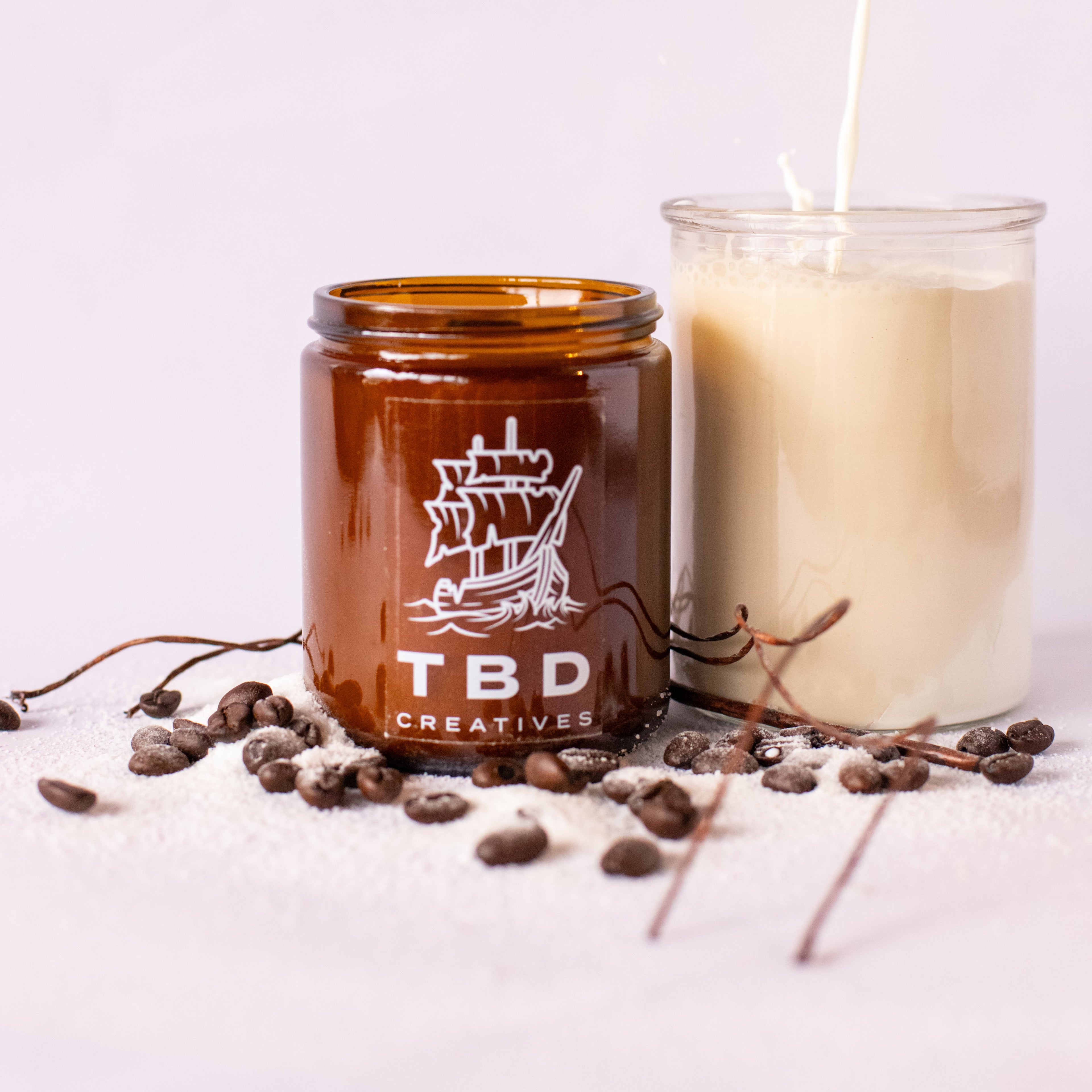 Two candles, one brown and one white, with 'TBD Creatives' branding on a light background.