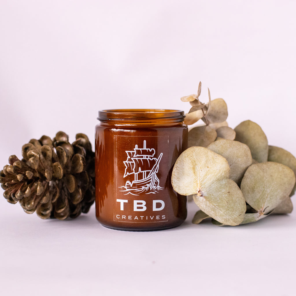Brown jar with 'TBD Creatives' logo surrounded by decorative elements on a white background