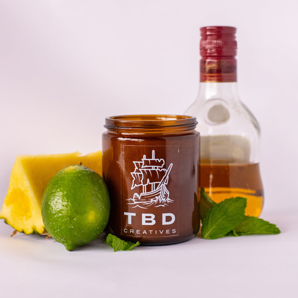 Jar of TBD Creatives with a bottle of alcohol, lime, and pineapple on a white background