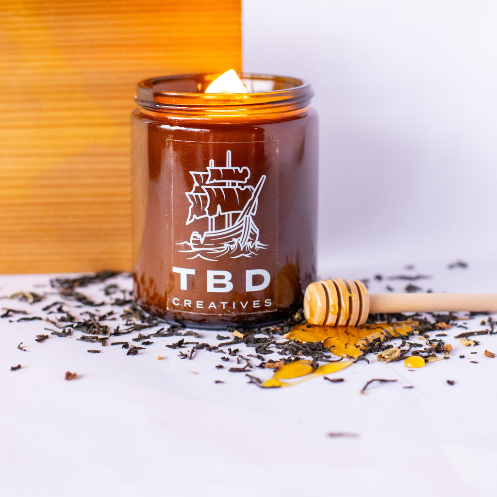 Candle in a glass jar with 'TBD Creatives' branding on a white background