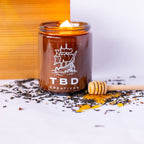 Candle in a glass jar with 'TBD Creatives' branding on a white background